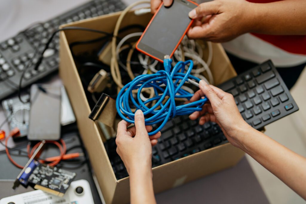Subscription-management-tools: Two people putting various waste electronic devices into a box for disposal