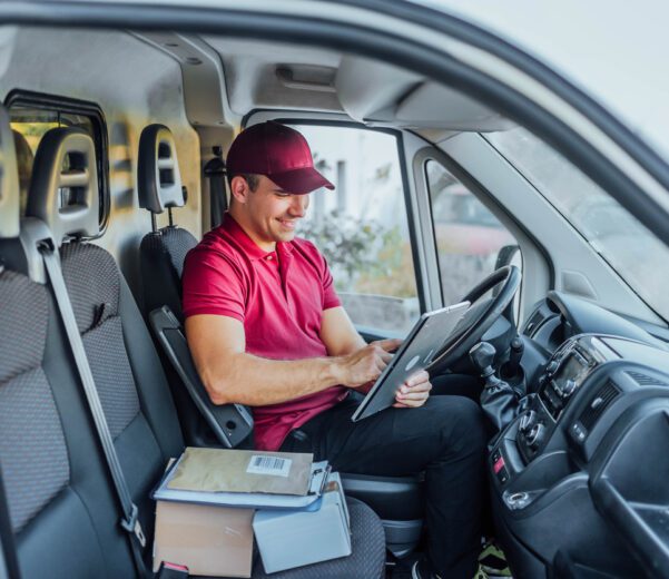 A food delivery person sits in truck using a tablet to access route optimization software.