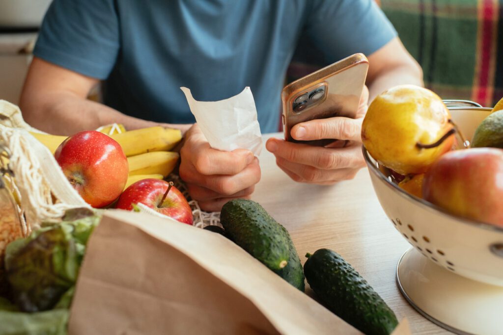 A man holding his smartphone while being surrounded by vegetables on the table.