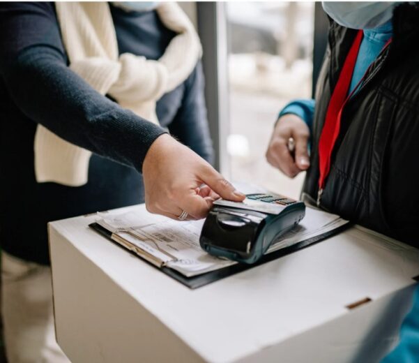 A customer taps a credit card on a portable payment terminal held by a delivery worker during a package drop-off.
