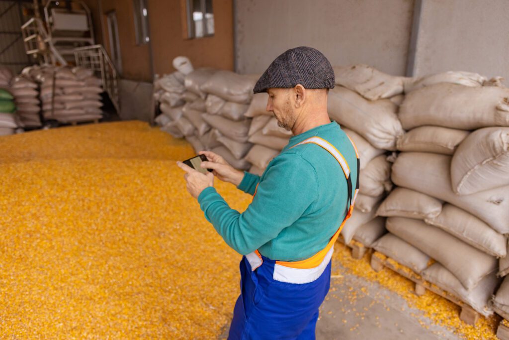 A farmer in his feed room uses his phone to access farming accounting software to monitor feed costs. 