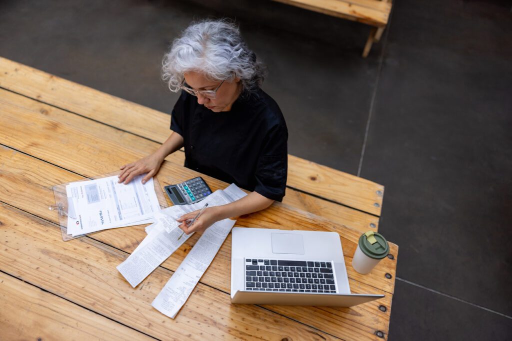 Farmer sits at a table, preparing taxes on her laptop with farming accounting software. 