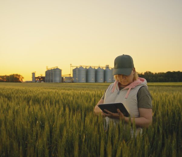 A female farmer stands in her field with her tablet, using technology to help her implement sustainable farming practices.
