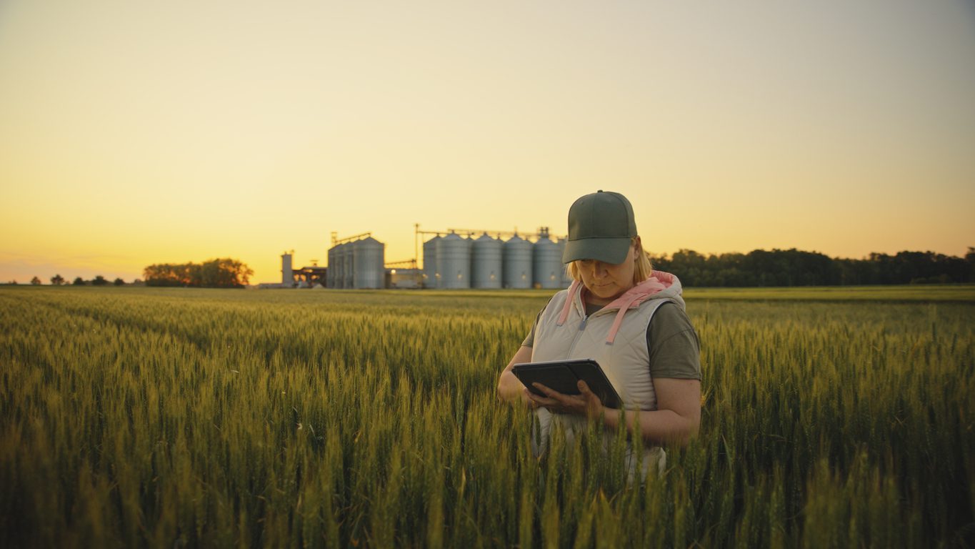 A female farmer stands in her field with her tablet, using technology to help her implement sustainable farming practices.