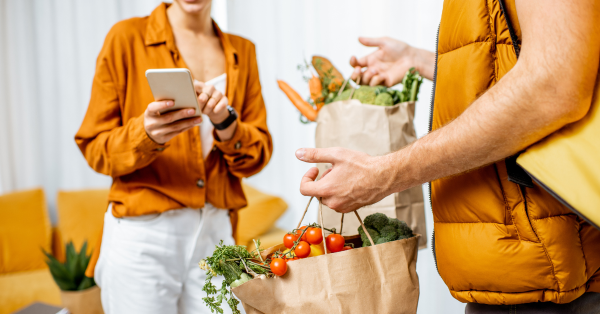Driver handing a paper bag of fresh vegetables to a customer at her door